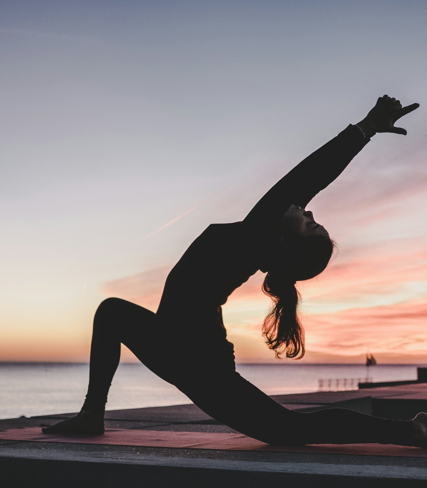 Person in einer seitlichen Yoga-Dehnung auf einer Matte bei Sonnenuntergang am Wasser
